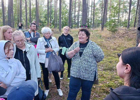 Grupa ludzi w lesie zgromadzona wokół jednej osoby opowiadającej.