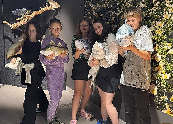 Grupa młodzieży,  trzymają  w rękach maskotki - ryby.